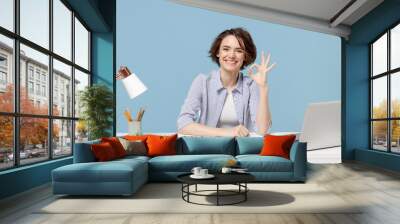 Young successful employee business woman in casual shirt sit work at white office desk with pc laptop show okay gesture isolated on pastel blue background studio portrait Achievement career concept Wall mural