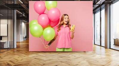 Young surprised amazed fun woman she wears shirt celebrating birthday holiday and hold bunch of colorful air balloons use mobile cell phone isolated on plain pastel pink background. Lifestyle concept. Wall mural