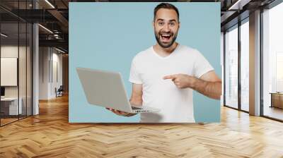 Young surprised happy fun man 20s wearing blank print design white t-shirt hold use work point index finger on laptop pc computer isolated on plain pastel light blue color background studio portrait Wall mural