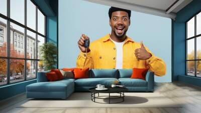 Young surprised man of African American ethnicity 20s wear yellow shirt hold car keys fob keyless system show thumb up isolated on plain pastel light blue background studio. People lifestyle concept. Wall mural