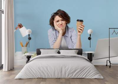 Young tired sleepy secretary employee business woman 20s in casual shirt sit work at white office desk with pc laptop hold paper cup of coffee prop up face isolated on pastel blue background studio Wall mural