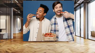 Young two friend men wear white casual shirts together holding italian pizza in cardboard flatbox eat biting slices look camera isolated plain dark royal navy blue background People lifestyle concept Wall mural