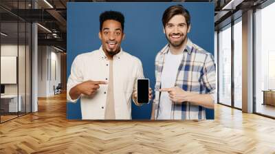 Young two friends men wear white casual shirts together use point finger on mobile cell phone with blank screen workspace area isolated plain dark royal navy blue background People lifestyle concept. Wall mural