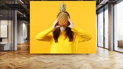 Young woman in casual clothes hiding, covering face with fresh ripe pineapple fruit isolated on yellow orange background in studio. People vivid lifestyle, relax vacation concept. Mock up copy space. Wall mural