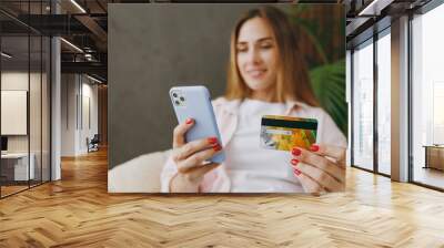 Young woman wear casual clothes sit in chair use mobile cell phone credit bank card shopping online order stay home hotel flat rest relax spend free spare time in living room indoor. Lounge concept. Wall mural