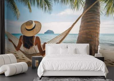 Woman Relaxing in a Hammock Between Palm Trees on a Beach. A person with sun hat lies in a hammock tied between two palm trees on a tropical sandy beach. Wall mural