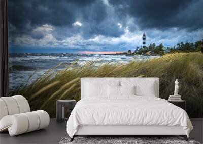 Thunderstorm over Baltic sea in a windy summer evening. Impressive waves hitting breakwater. Lighthouse covered in dark storm clouds above. Sandy seashore covered in tall grass. Wall mural