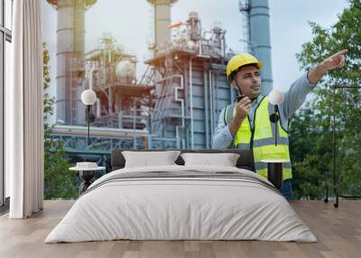 worker talking on the radio communication. industrial engineer in Oil factory. Engineer wearing PPE uniform and helmet looking detail tablet on hand with power plant  on background. Wall mural