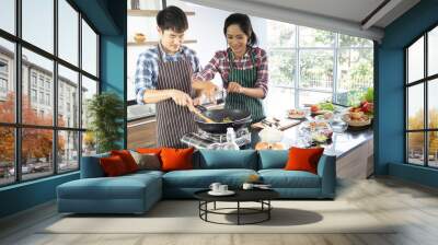 Young Asian couple are happy to cook together, two families are helping each other prepare to cook in the kitchen. Wall mural