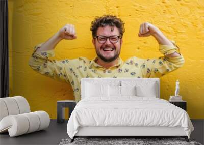 A person posing with flexed muscles, dressed in a yellow shirt and wearing glasses Wall mural