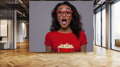 A woman wearing red glasses holds a bucket of freshly popped popcorn, perfect for movie night or game day Wall mural