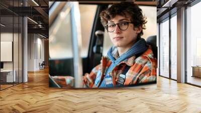 A young adult male sits in a vehicle, wearing glasses Wall mural