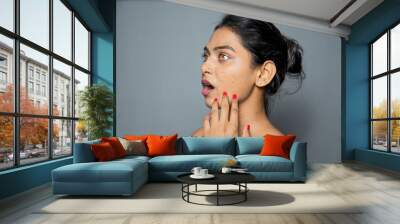 Indian beautiful young woman worrying side face about her pimples, acne and dark spots on skin. beauty and skincare concept isolated on gray background Wall mural