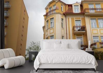 There is a bright yellow building featuring a balcony situated on one side of it, contributing charm to the overall architectural design Wall mural