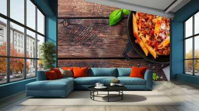  A pan of pasta with tomato sauce and basil on a worn wooden table Nearby, a slice of bread and tomatoes rest Wall mural