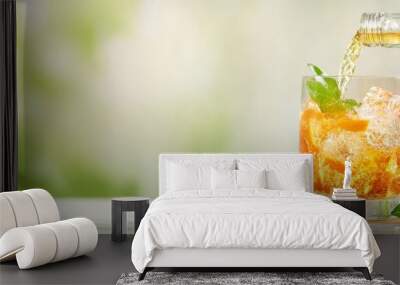  A pitcher pours tea over ice-filled glass Garnished with mint and orange slices Wall mural