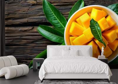  A white bowl, brimming with sliced mangos, rests on a weathered wooden table Nearby, vibrant green leaves unfurl Wall mural