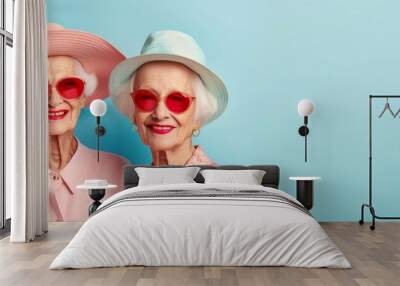  Two older women in red heart-shaped sunglasses and a pink hat stand against a blue backdrop Wall mural