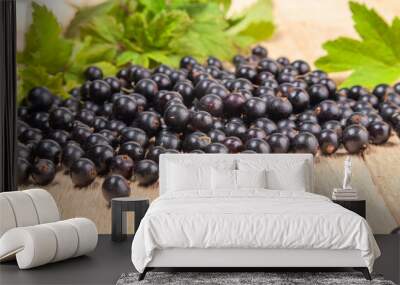 Fresh ripe black currants heap on wooden background. Natural organic berries with green leaves scattered on weathered wooden table, new berry harvest. Wall mural