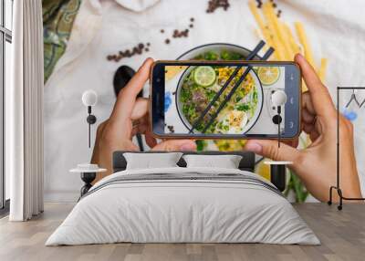 Smartphone food photography. Woman hands take phone photo. Ramen noodle soup with egg, corn and meat in bowl. Asian Thai traditional authentic food with vegetables served in cafe or restaurant Wall mural