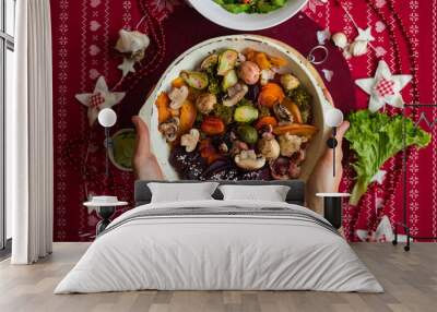 Woman hands hold skillet with baked, roasted, grilled vegetables. Beetroot, carrot, mushrooms, pumpkin, brussels sprouts with avocado dpi sauce. Vegan lunch, vegetarian Christmas food, red tablecloth Wall mural