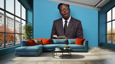 African man in suit holding and counting money. Studio shot on blue wall. Wall mural