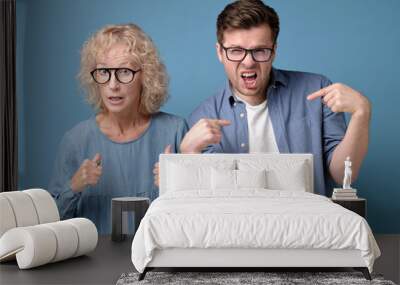 Displeased caucasian man and woman, dressed in casual clothes, pointing with index fingers saying are you blaming us for your mistake. Wall mural