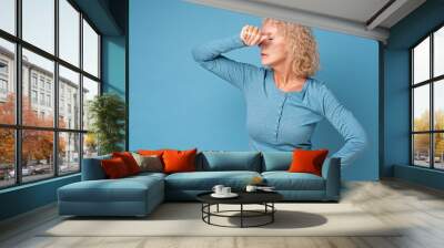 Mature caucasian woman suffering a headache or insomnia having no power. Studio shot on blue wall. Wall mural