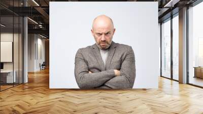 Portrait of offended european man in suit holding hands crossed on chest, looking from under forehead Wall mural