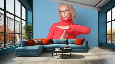 Senior caucasian woman in red sweater and glasses making time out gesture. I need a pause. Do not be in a hurry. Studio shot Wall mural