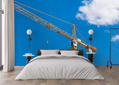 Yellow tower crane with white cab against blue sky. Wall mural