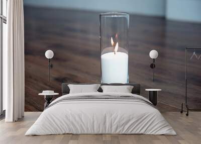 A burning candle in tall glass vase flask standing on the floor in the middle of room. Wall mural