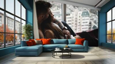 Beautiful romantic couple hugging against the background of a large bright window. attractive man cuddle brunette in shirt and stockings. portrait of lovers in a cozy atmosphere Wall mural