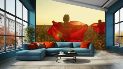 Children dreams of becoming superhero. Kids in red cloak, sun. Happy girl, boy play superheroes they run across yellow field in red cloak, cloak flutters in wind. Childrens games, dreams. Slow motion Wall mural