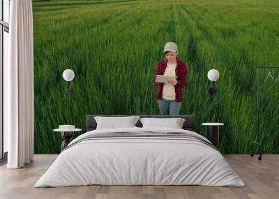 Farmer woman working with computer tablet on green growing wheat field. Woman hand touch ears of green young wheat . Growth young wheat. Concept growing organic food, agricultural business development Wall mural