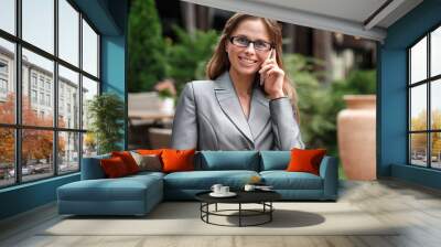 Business woman in eyeglasses standing on the city street talking on smartphone looking camera happy Wall mural