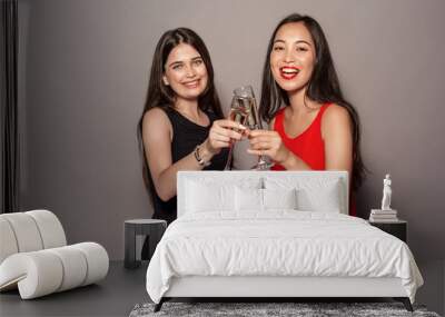 Freestyle. Young girls in dresses standing isolated on gray cheers with glasses of champagne smiling joyful Wall mural