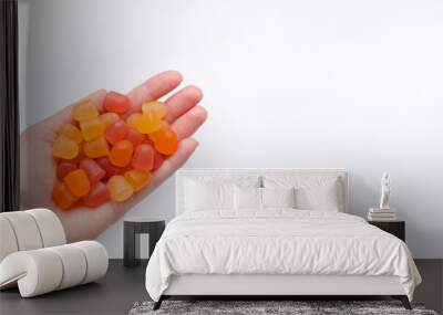 Group of red, orange and yellow multivitamin gummies in the hand isolated on white background Wall mural