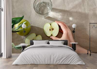 Hand holding half of green apple. Fresh fruits and glass of water on table, healthy nutrition concept Wall mural