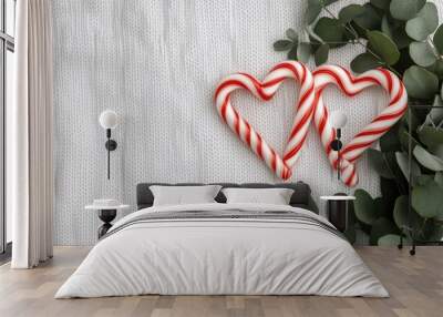 Two candy cane hearts rest on a soft white knit fabric, accompanied by pine branches and scattered orange peels, creating a warm and festive atmosphere Wall mural