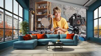 Make-up Blogger. Young woman sitting at stylish apartment recording video on camera applying bronzer on cheeks looking at mirror happy Wall mural