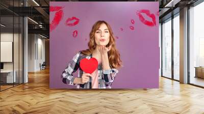 Valentine's Day. Stylish woman studio standing isolated on grey with heart shape card sending air kiss to camera joyful Wall mural