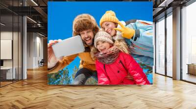 Winter vacation. Family time together outdoors taking selfie on smartphone grimacing to camera playful bottom view Wall mural