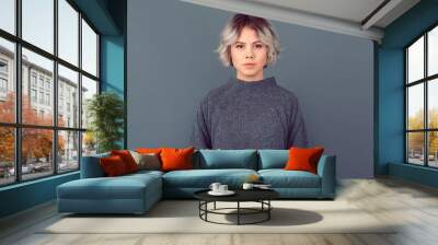 Young woman in a grey sweater studio picture isolated on grey background serious Wall mural