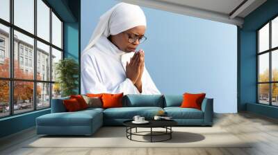 Serene African Nun Praying in Contemplation Against Blue Background Wall mural