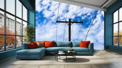 A wooden utility pole with electrical wires standing against a deep blue sky with white clouds.  Wall mural