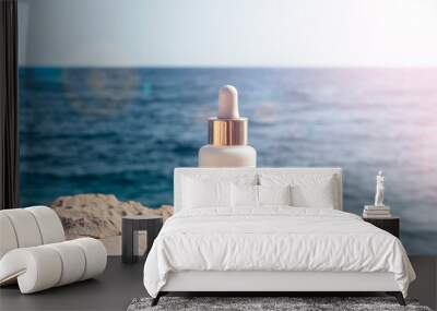 Cosmetic serum bottle on stone on the background blue sea in sunlight, closeup Wall mural