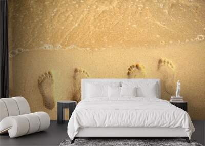 Feet prints on the sand of the beach and sea wave. Top view. Two people foot marks on sand.  Wall mural