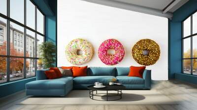 Three colorful donuts on a white wooden background. Wall mural