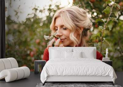 beautiful woman farmer sniffs a freshly picked apple and smiles cute in background of the garden Wall mural